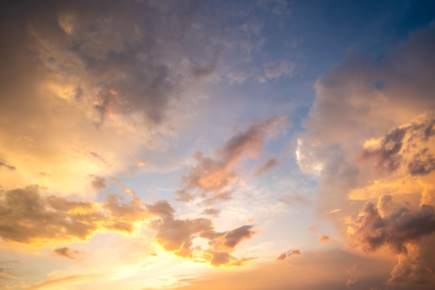 Dramatic cloudy sunset landscape with puffy clouds lit by orange setting sun and blue sky