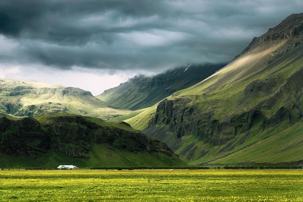 Dramatic Icelandic mountain with sunlight shining through storm clouds and house on field in summer at Iceland