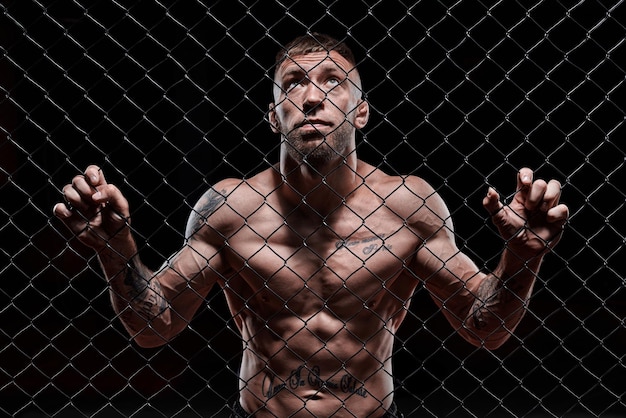 Dramatic image of a mixed martial arts fighter standing in an octagon cage Powerful abdominal muscles The concept of sports boxing martial arts