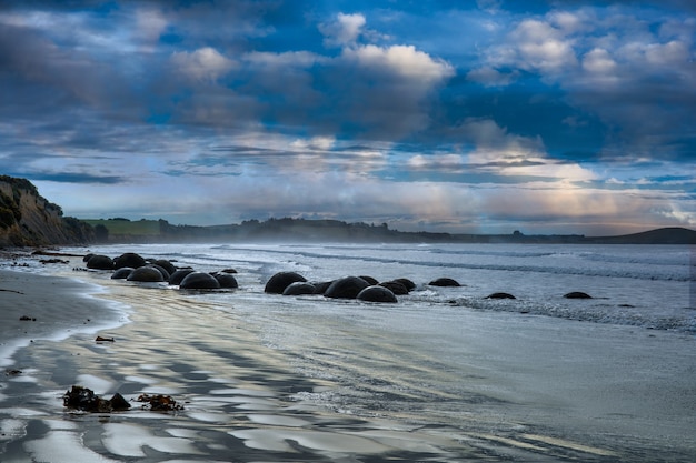 Dramatic moody blue cloudscape reflecting blue tones on the Dunedin beach and its iconic boulder formations