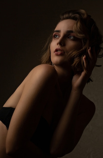 Dramatic portrait of amazing brunette model with wavy hair wears bra, posing in the shadows