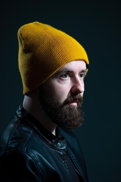 Dramatic portrait of a millennial guy in a yellow hat and jacket on a dark background