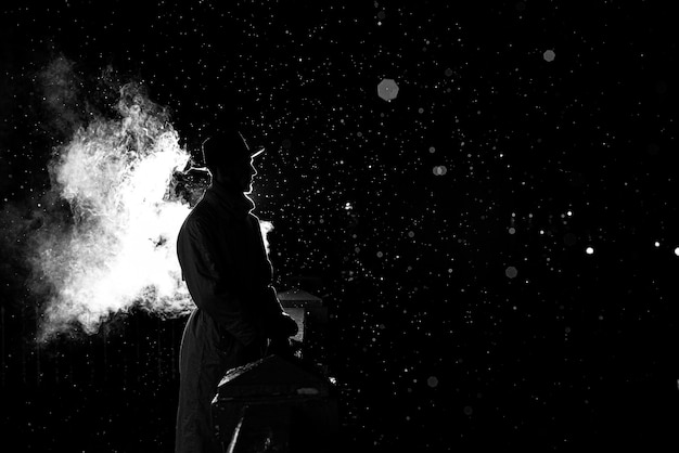 Dramatic silhouette of a dangerous man in a hat at night in the rain in the city in the old crime Noir style