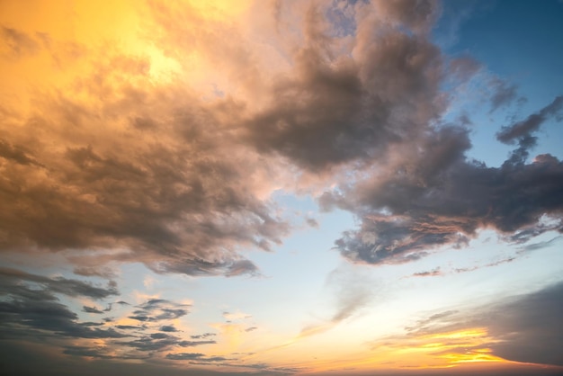 Dramatic sky at sunset with puffy clouds lit by orange setting sun