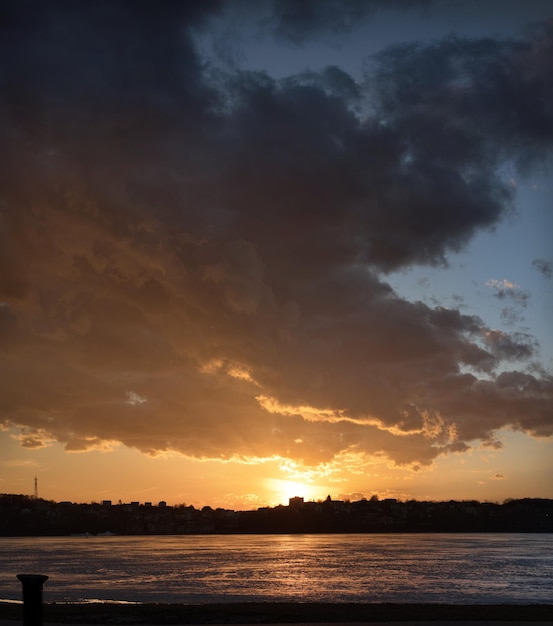 Dramatic sky with cloud over frozen lake silhouettes of shore and reflection of sunset on ice