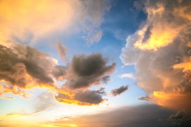 Dramatic sunset landscape picture with puffy clouds lit by orange setting sun and blue sky.