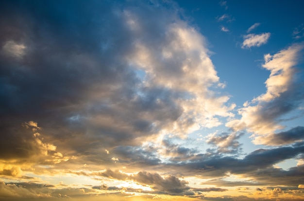 Dramatic sunset landscape with puffy clouds lit by orange setting sun and blue sky.