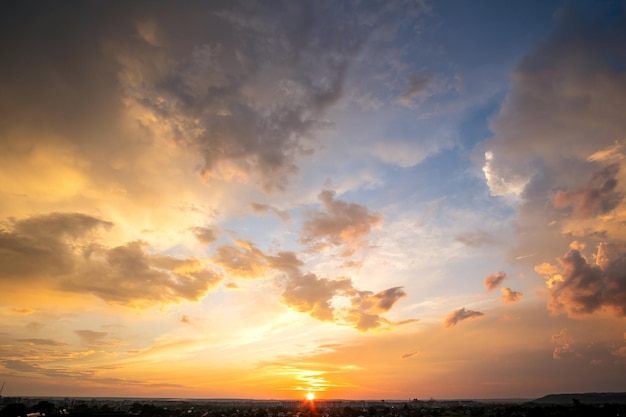 Dramatic sunset landscape with puffy clouds lit by orange setting sun and blue sky.