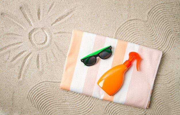 Photo drawing on the sand sun and wavessunglasses with an orange bottle beach towel sun spray on the sand