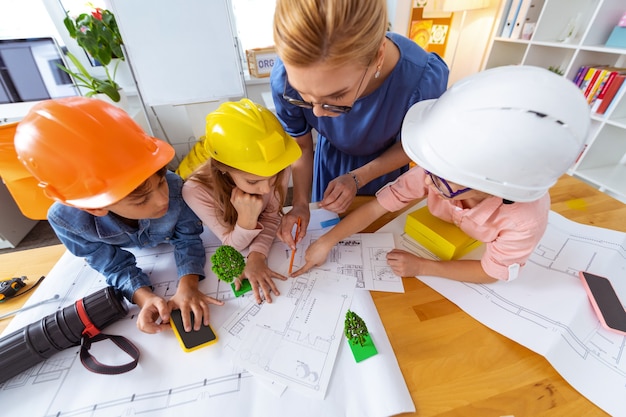 Drawing sketches. Two boys and girl wearing bright helmets drawing sketches with their teacher