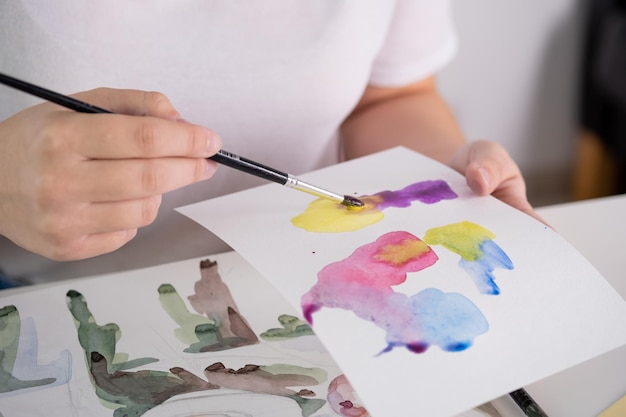 Drawing in watercolor on a white sheet A young woman paints in watercolor at home on a white sheet