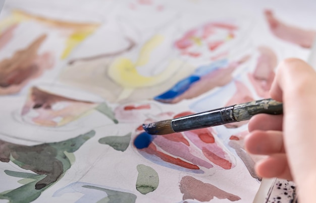 Drawing in watercolor on a white sheet A young woman paints in watercolor at home on a white sheet