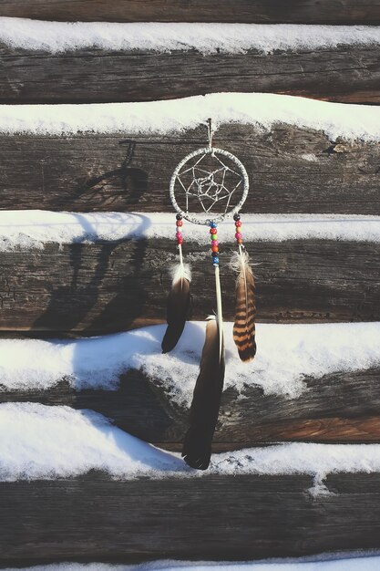 Photo dream catcher on old wooden snow covered wall background. homemade decor with beads and feathers.