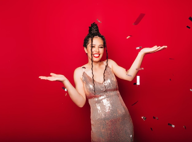 A dream a dreamy concept A beautiful attractive modern lady with dreadlocks catches confetti isolated on a red backgroundholiday and birthday concept