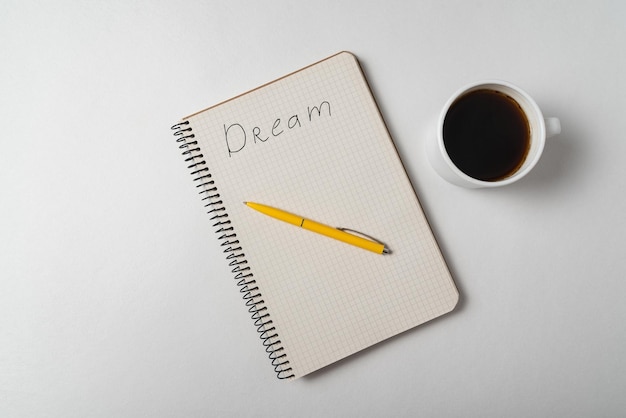 Dream reminder notice Copybook with pen and cup of coffee on white background Top view