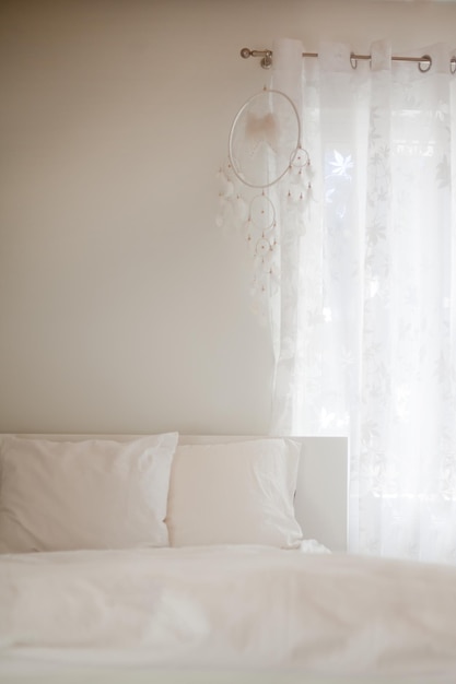 Dreamcatcher with thread feathers at white bedroom place for text selective focus