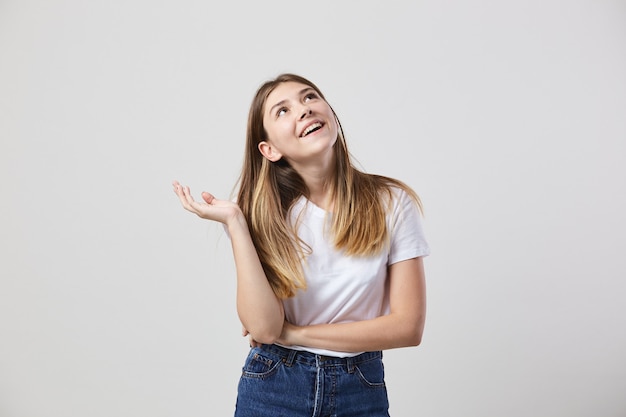 Dreaming girl dressed in a white t-shirt and jeans is on a white background in the studio .