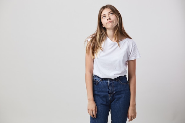 Dreaming girl dressed in a white t-shirt and jeans is on a white background in the studio .