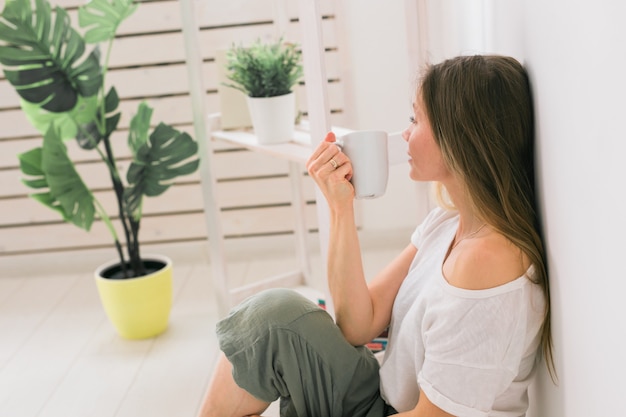 Dreaming girl sitting on floor at home and drink tea from cup