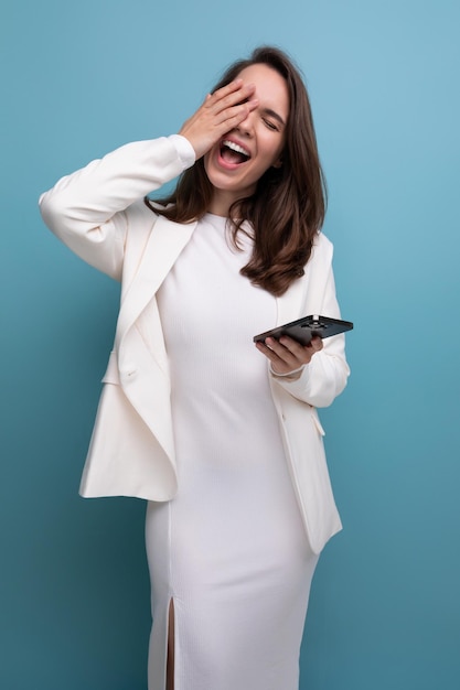 Dreaming woman with dark long hair in an elegant white dress holding a phone in her hands