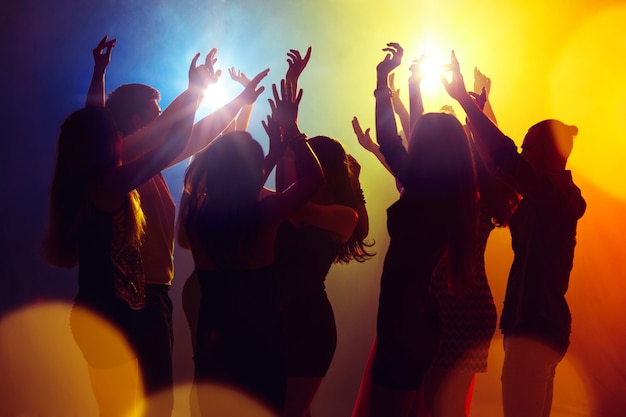 Dreams. A crowd of people in silhouette raises their hands on dancefloor on neon light background. Night life, club, music, dance, motion, youth. Yellow-blue colors and moving girls and boys.