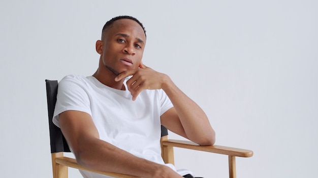 Dreamy athletic relaxed black young man sitting on a armchair against white wall