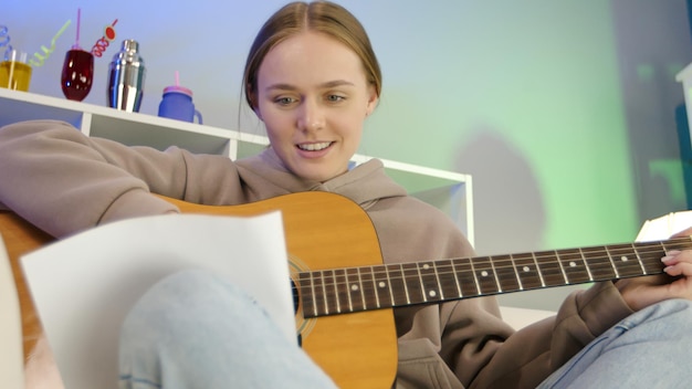 Dreamy girl playing acoustic guitar at home Female musician learning to play musical instrument