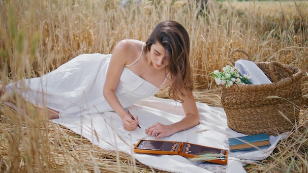 Dreamy girl sketching album relaxing blanket at rye landscape model drawing