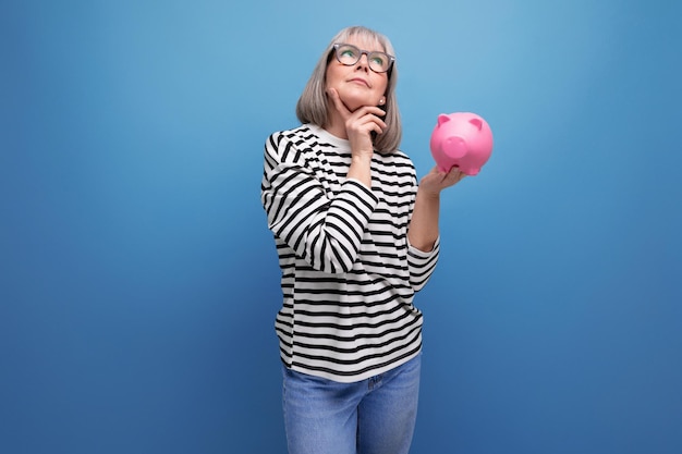 Dreamy grandmother middleaged woman holding a piggy bank with savings on a bright background with