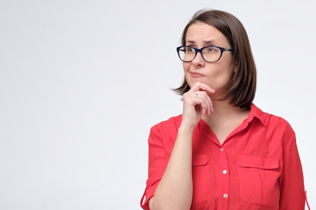 Dreamy mature woman looking thoughtfully aside holding her finger on chin