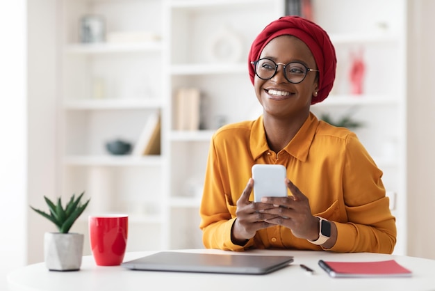 Dreamy stylish black woman using mobile phone and smiling