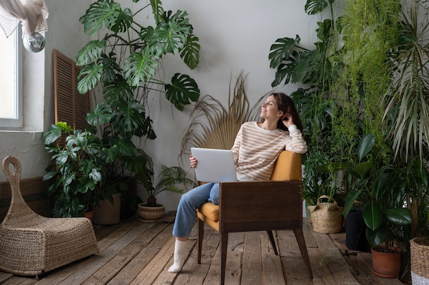 Dreamy woman rest after finished work on laptop look in window sitting in chair at cozy home garden