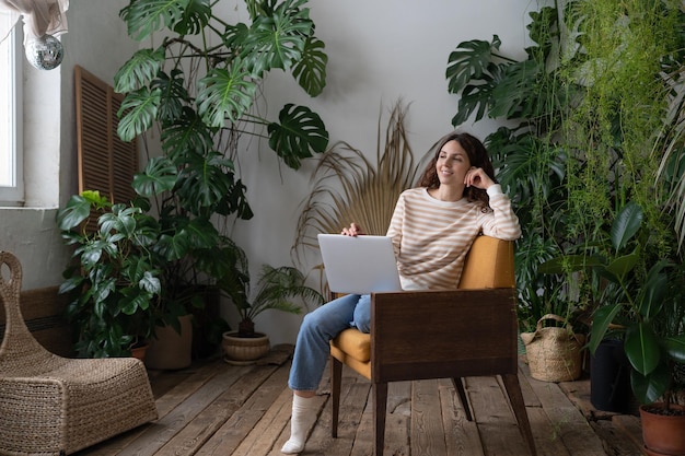 Dreamy woman rest after finished work on laptop look in window sitting in chair at cozy home garden