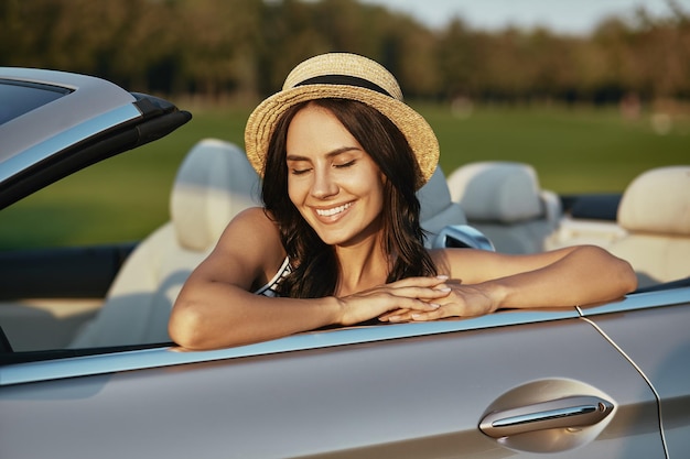 Dreamy woman sitting in luxury cabrio with closed eyes