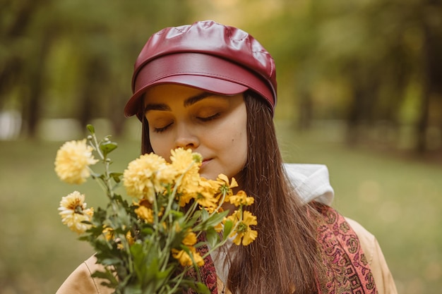 Dreamy woman smelling bouquet of yellow flowers in autumn park