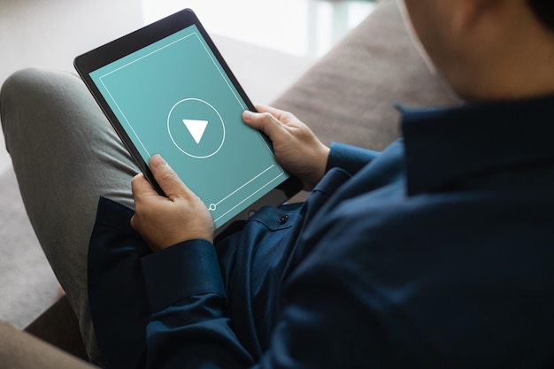 Dressed man watching video on tablet sitting on sofa in house