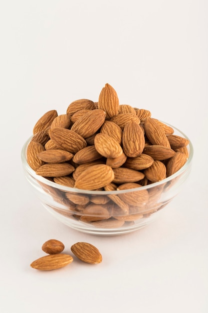 Dried almonds in a glass bowl, side view on a light background. A natural product for the diet. Vertical orientation.