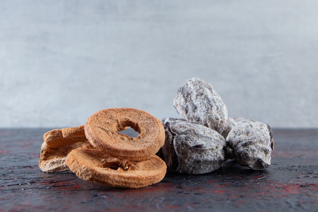 Dried apple rings and tasty persimmons on dark background.