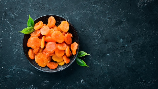 Dried apricots in a bowl on a black background. Top view. Free space for your text.