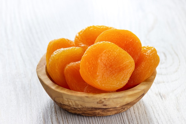 Dried apricots in a bowl on light wooden background.