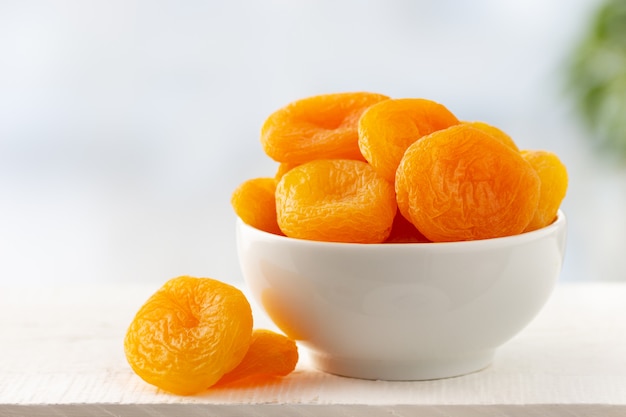 Dried apricots in a bowl on light wooden