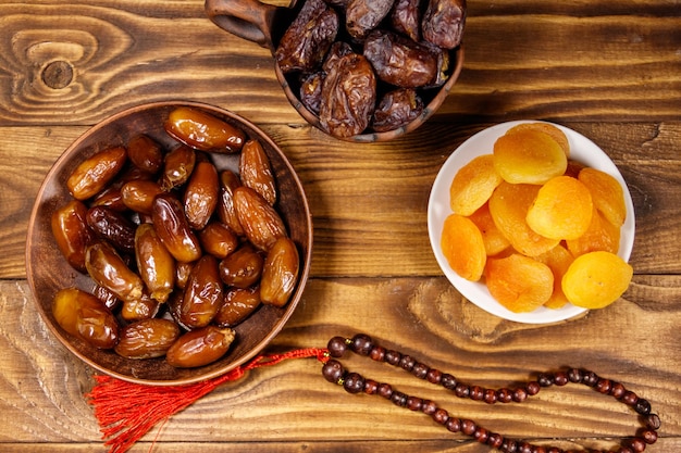 Dried apricots and dates fruit with wooden rosary on wooden table Top view