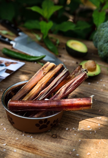 Dried  beef penises in the dog vessel  on the wooden board and some knives and vegetables on the background. Chewing treats for domestic dogs. 