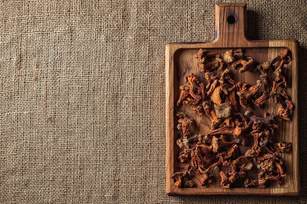 Dried chanterelle mushrooms (CantharÃÂllus cibÃÂrius), on a wooden board, on a rough woven surface, burlap, top view