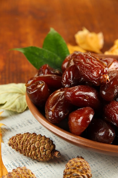 Dried dates on plate with yellow leaves on wooden background