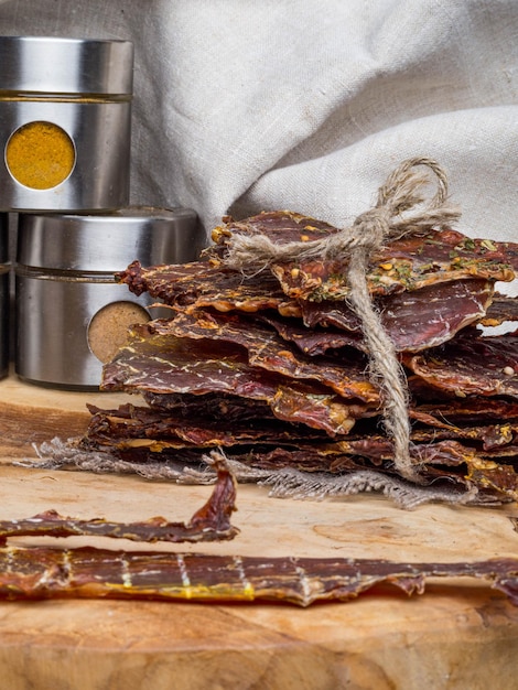 Dried or dehydrated meat slices with spices in jars on wooden background copy space