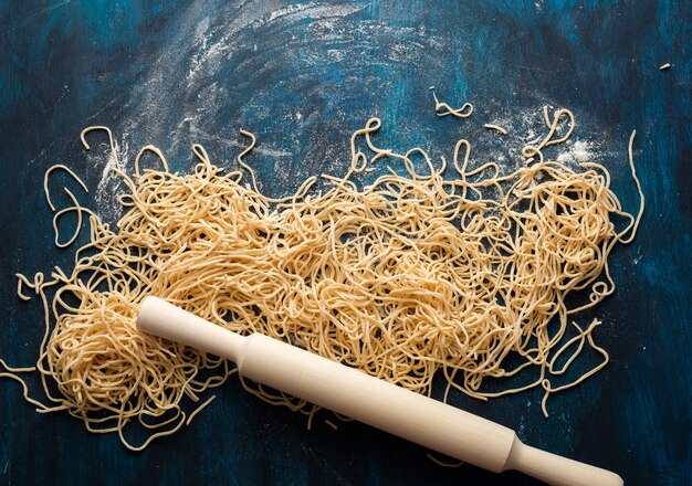 Photo dried egg noodles, raw fresh spaghetti on blue wooden background, top view