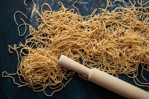 Photo dried egg noodles, raw fresh spaghetti on blue wooden background, top view