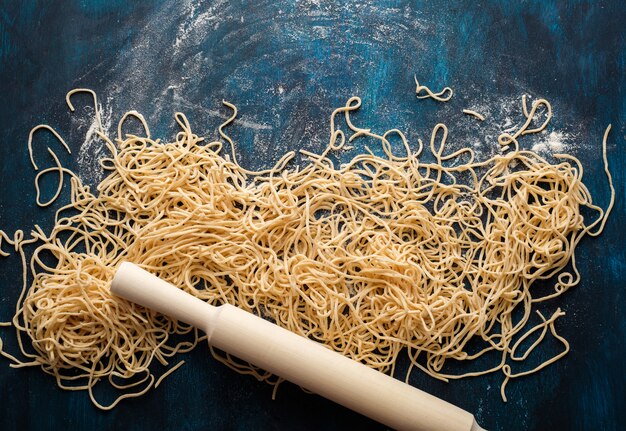 Photo dried egg noodles, raw fresh spaghetti on blue wooden background