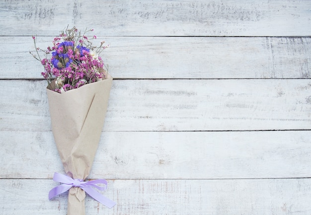 Dried flower bouquet in brown paper on wood background.